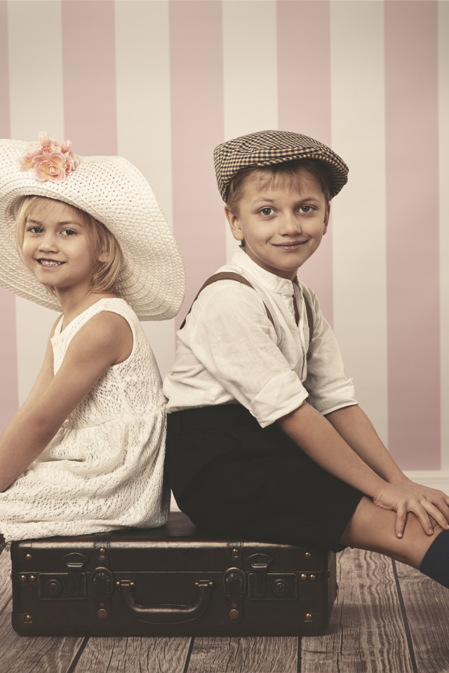 Девочка в большой белой шляпе и мальчик сидят на чемодане
