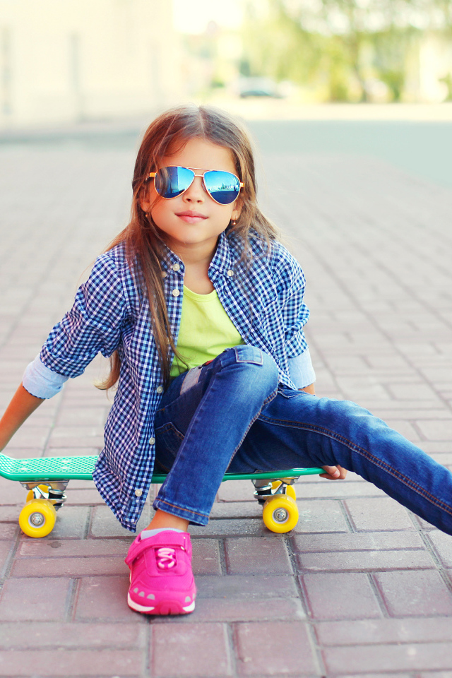 Девочка в солнечных очках сидит на скейтборде