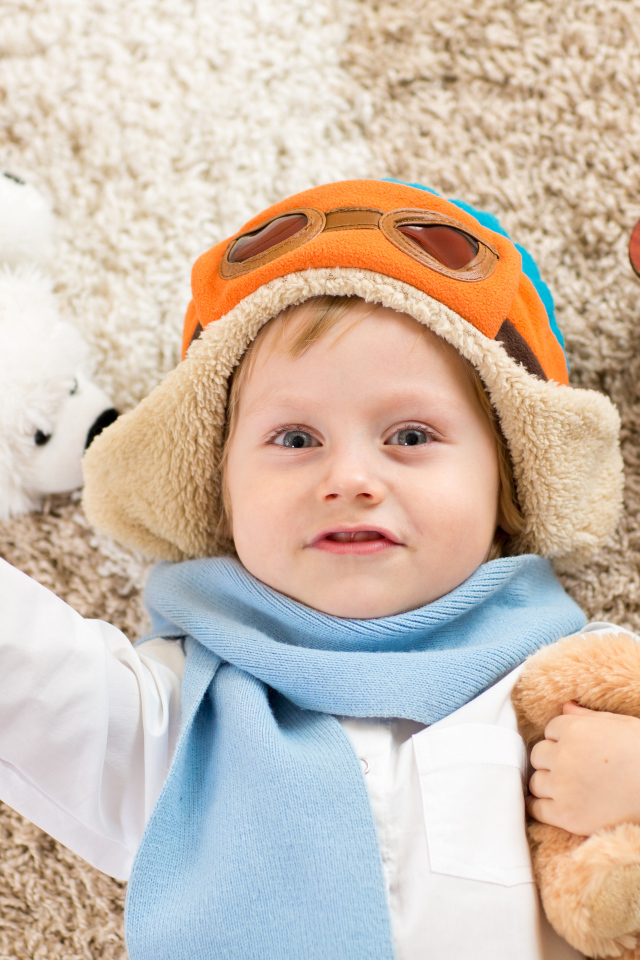 Маленький мальчик в шапке и игрушечным самолетом и медвежонком в руках