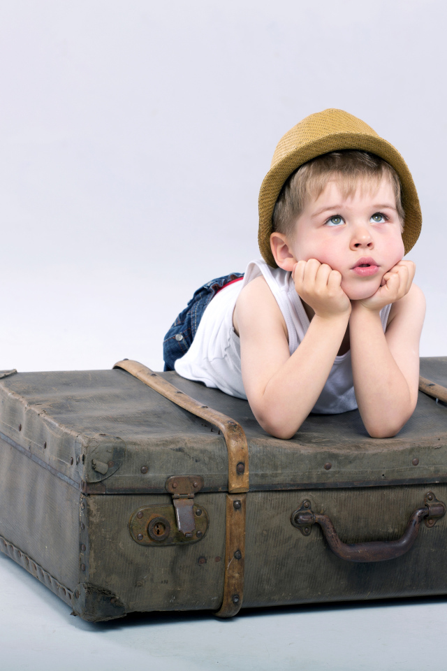 Маленький мальчик лежит на большом чемодане на сером фоне