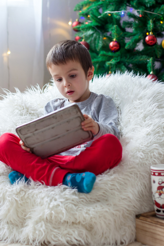 Маленький мальчик сидит в мягком кресле у новогодней елки