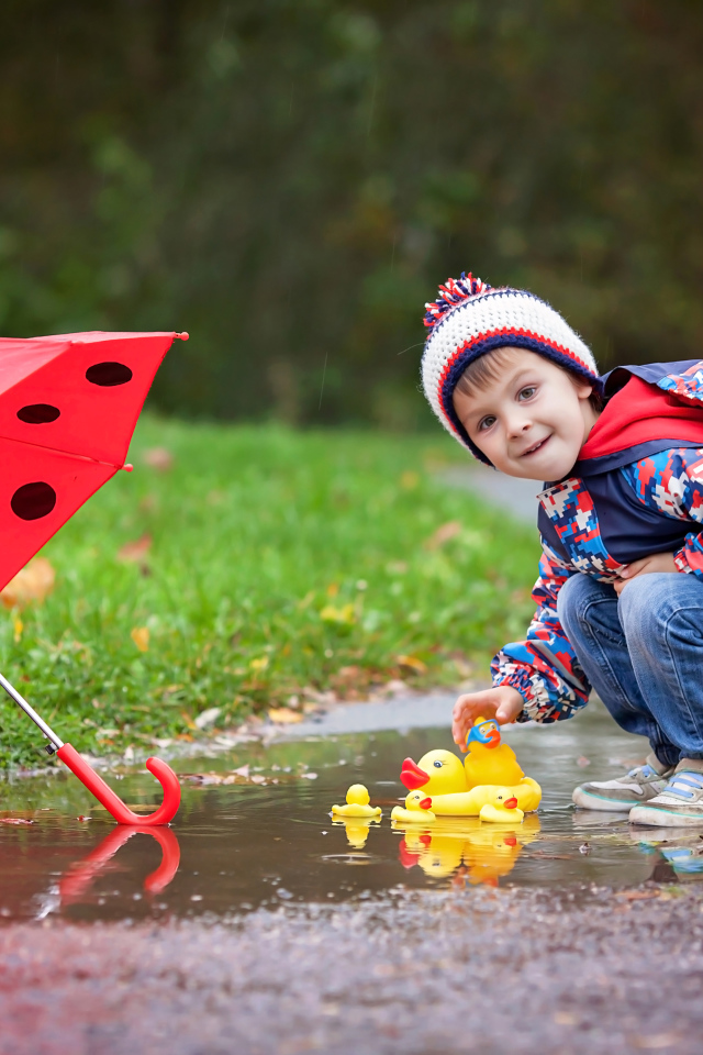 Маленький мальчик пускает резиновую уточку в лужу после дождя