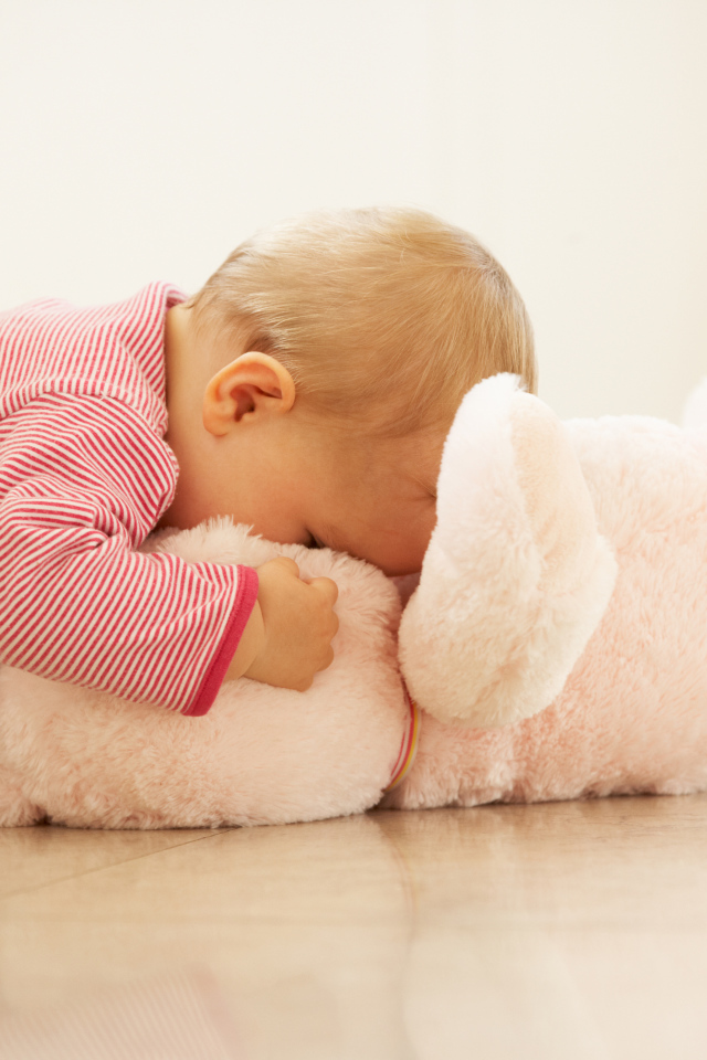 Маленький ребенок играет с розовым плюшевым мишкой