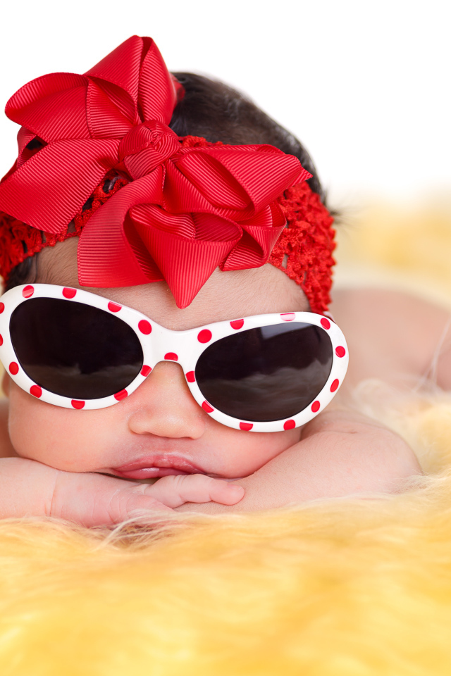 Маленькая забавная малышка в очках и с красным бантом на голове