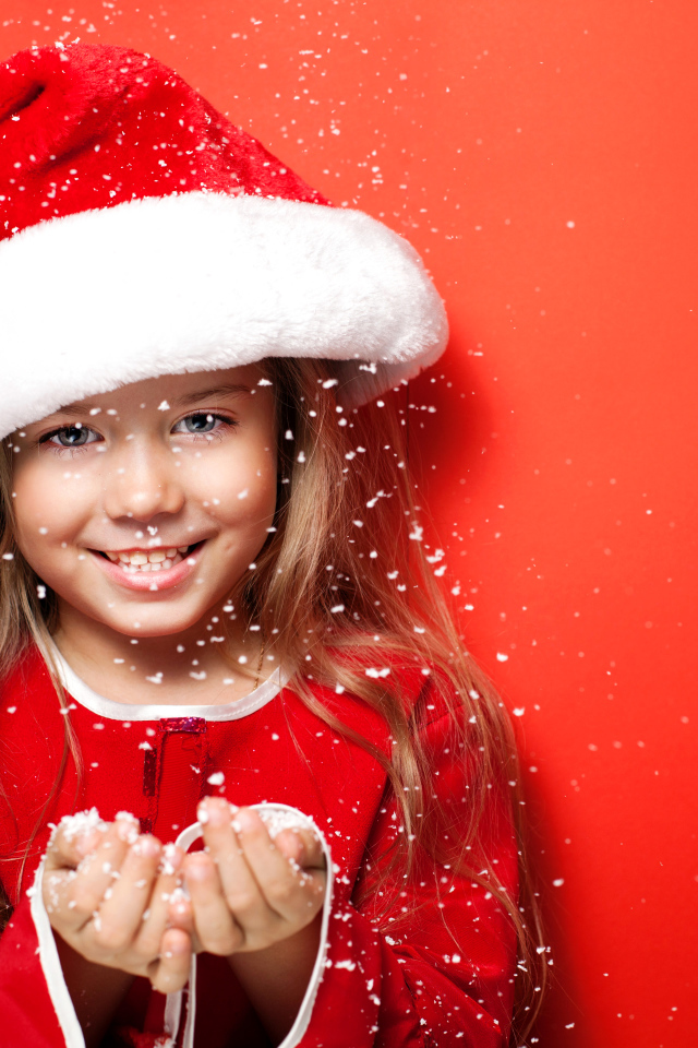 Маленькая девочка в новогодней шапке ловит руками снежинки