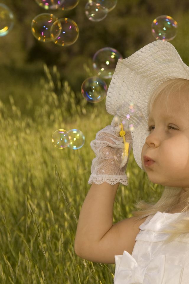 Маленькая девочка в большой белой шляпе пускает мыльные пузыри