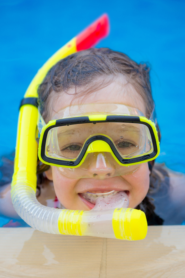 Маленькая девочка в маске с трубкой плавает в бассейне