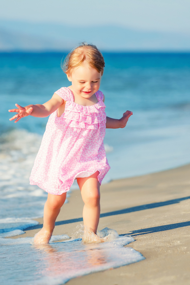 Маленькая девочка в розовом платье гуляет по морскому песку