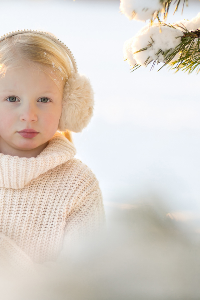 Маленькая девочка в белом свитере у покрытой снегом ели