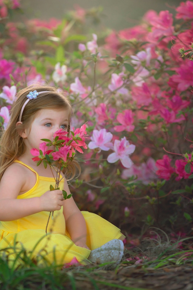 Маленькая девочка в желтом платье сидит рядом с розовыми цветами