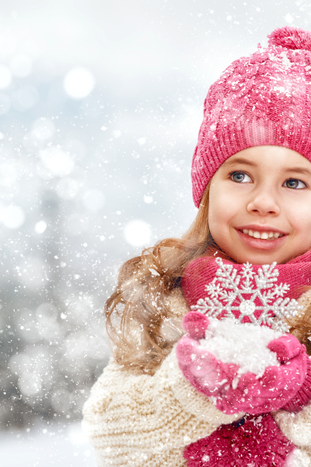 Маленькая девочка в зимней одежде держит снег в руках