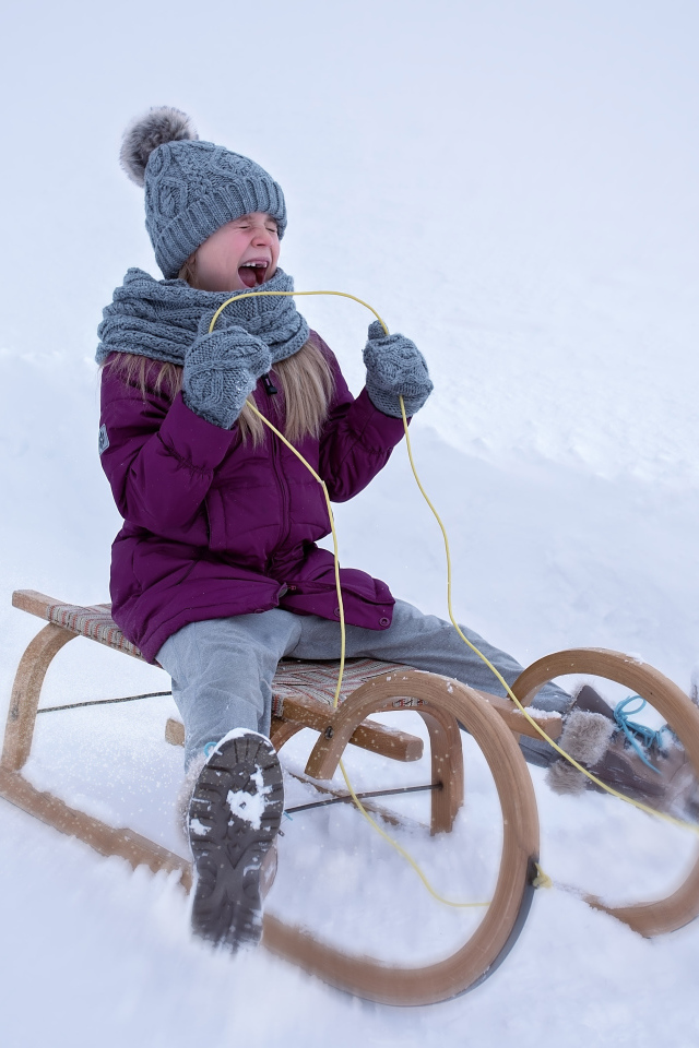 Маленькая девочка едет на санях с горки зимой