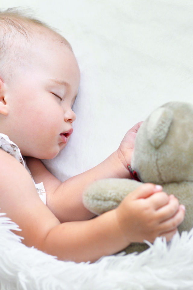 Маленькая девочка спит с мягкой игрушкой под белым одеялом