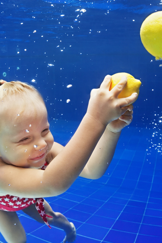 Маленькая девочка плавает в бассейне с желтыми лимонами