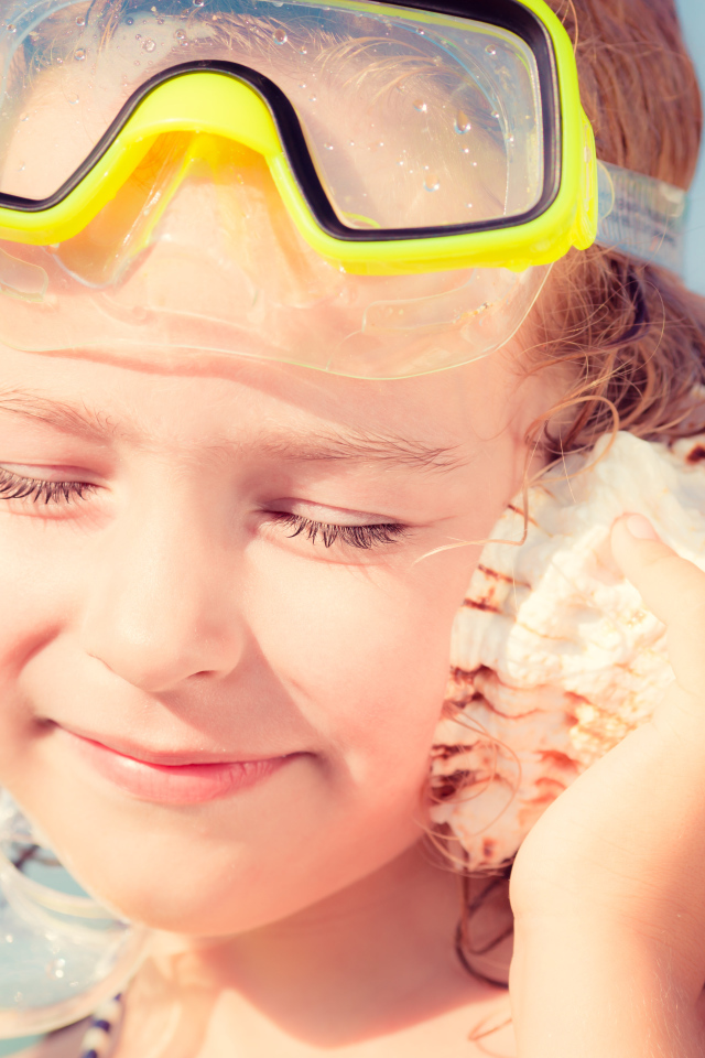 Маленькая девочка приложила ракушку к уху