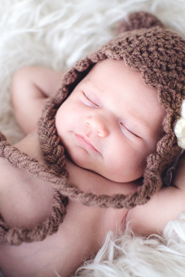 Спящий грудной ребенок в коричневой вязаной шапке с белым цветком