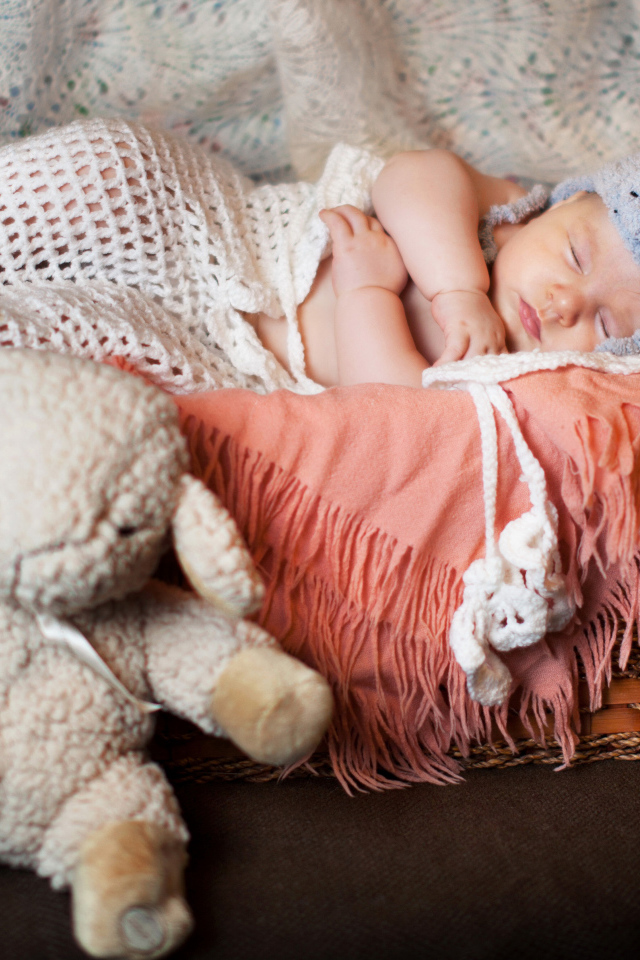 Спящий грудной ребенок в забавной шапке с мягкой игрушкой