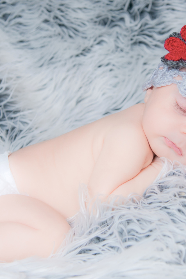 Спящий грудной ребенок в вязаной шапке с красным цветком на голове