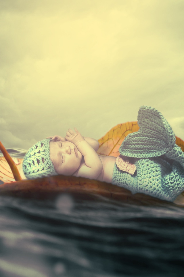 Маленький грудной ребенок в костюме русалки плывет на листе в океане