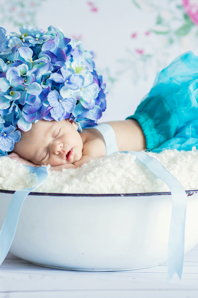 Маленький грудной ребенок спит в миске с шапкой из цветов гортензии на голове