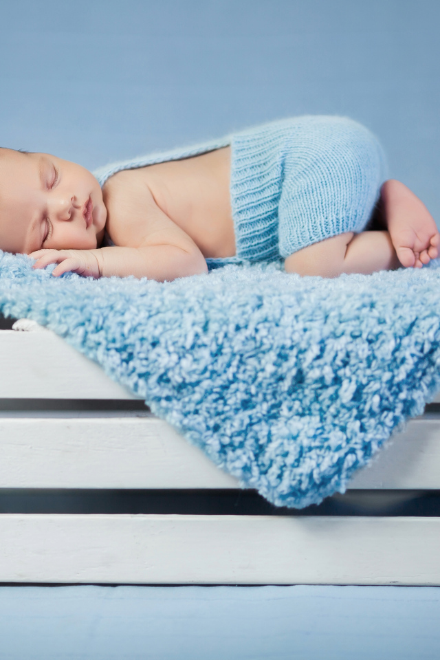 Маленький грудной ребенок спит на синем покрывале на деревянном ящике