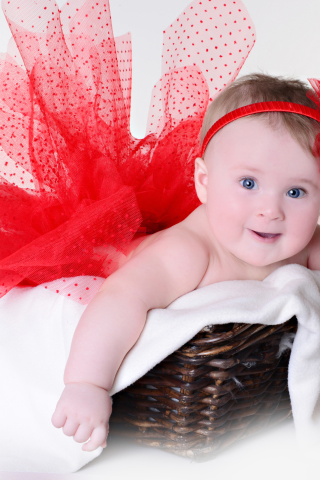 Маленькая голубоглазая девочка в красном красивом платье лежит в корзине