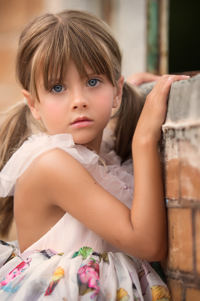 Милая девочка с серьезным взглядом стоит у стены