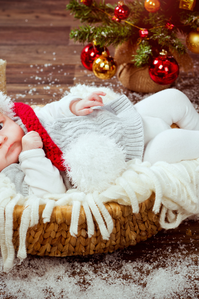 Младенец в корзине в новогоднем костюме под елкой с подарками