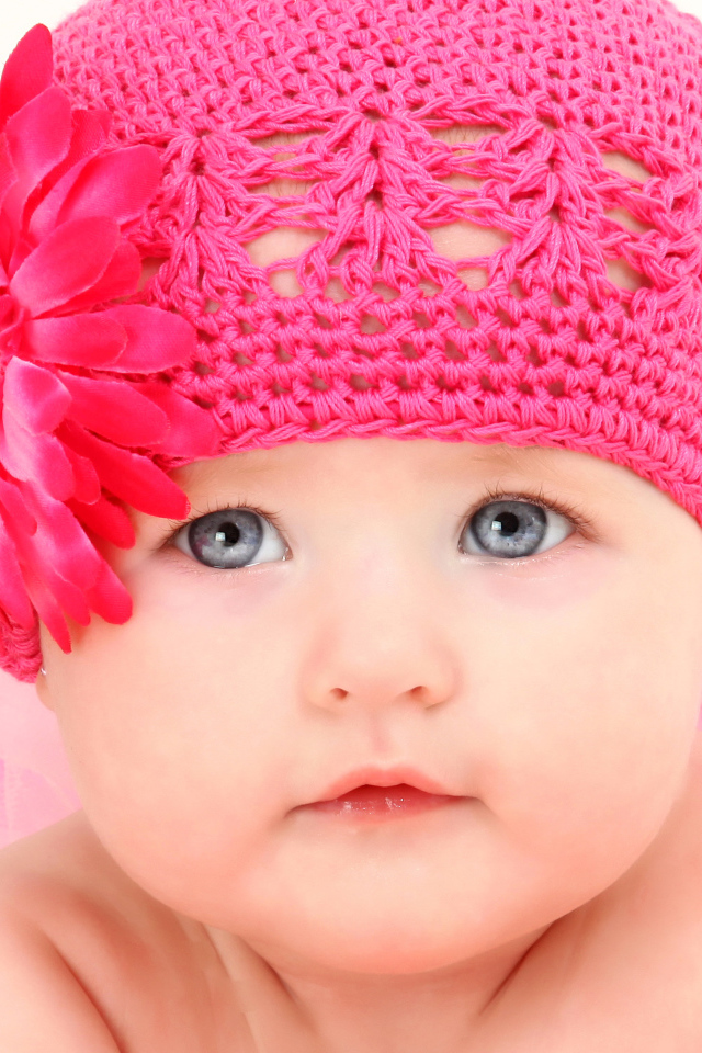 Милая голубоглазая малышка в розовой шапке с цветком герберы