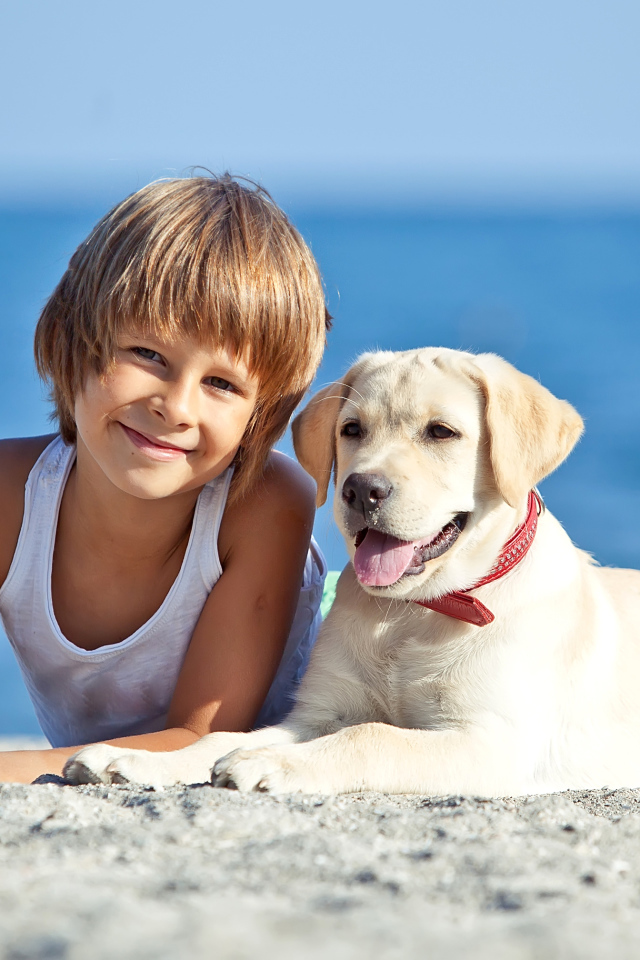 Симпатичный мальчик со щенком ретривера лежат на песке на пляже