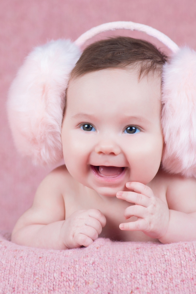 Милый улыбающийся младенец в больших розовых наушниках