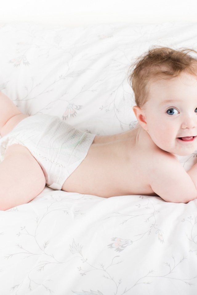 Забавный голубоглазый малыш лежит на белом покрывале