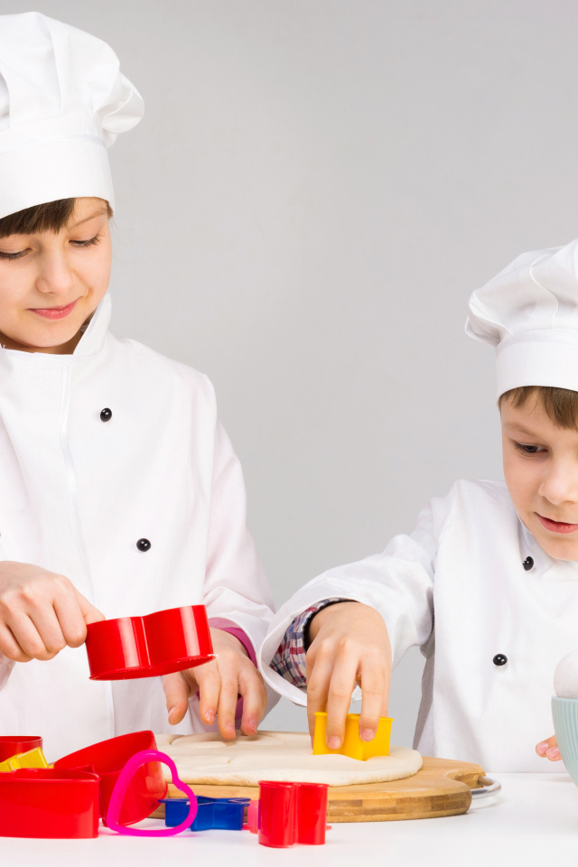 Маленькие мальчик и девочка готовят на кухне печенье