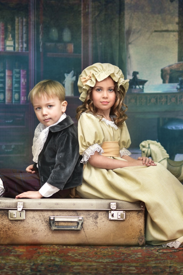 Маленькие мальчик и девочка в винтажных костюмах сидят на чемодане
