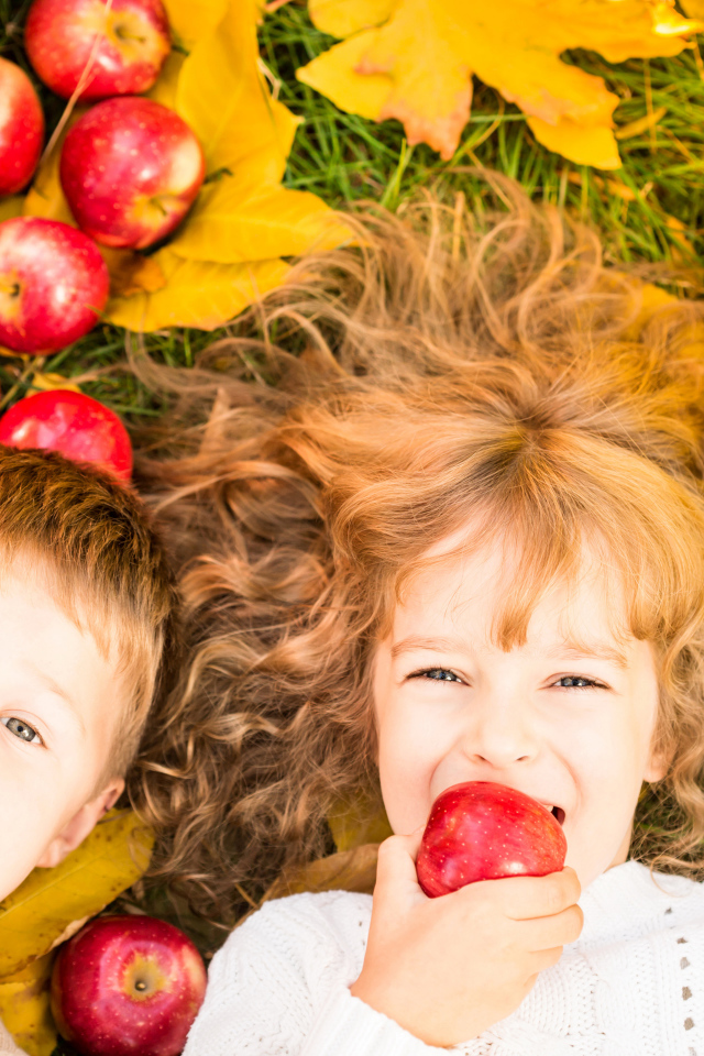 Маленькие мальчик и девочка лежат на желтой листве с красными яблоками