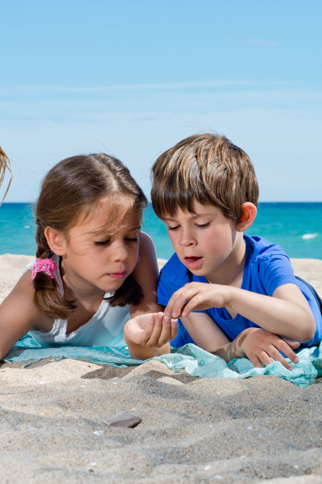 Маленькие мальчик и девочка играют на песке у моря