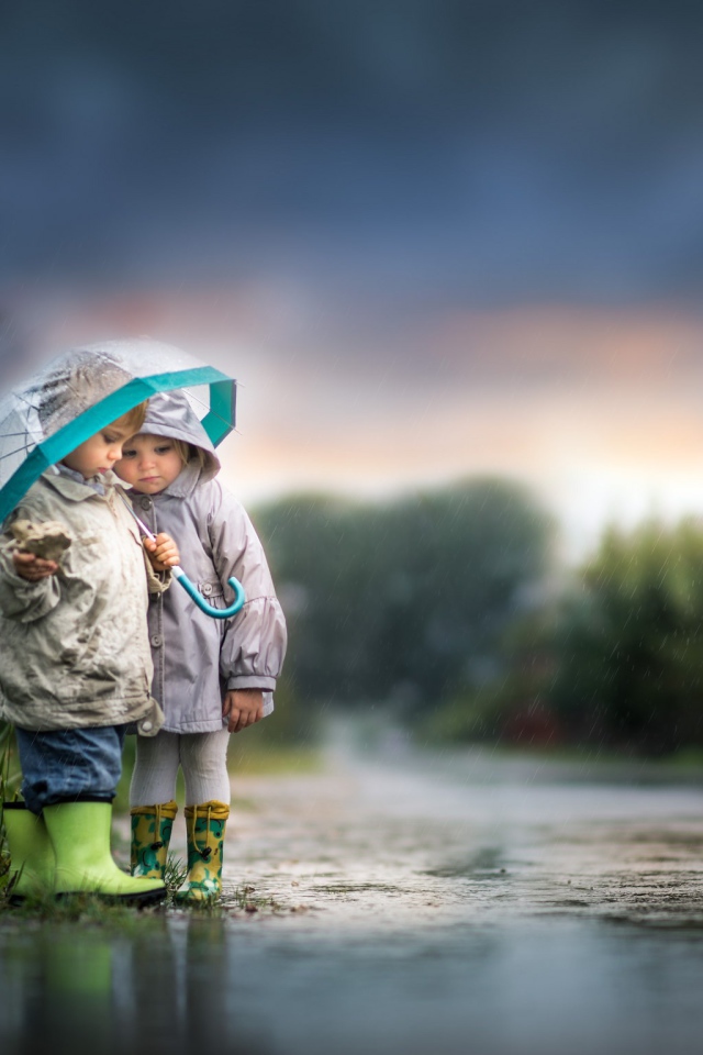 Маленькие мальчик и девочка под зонтом на дороге 