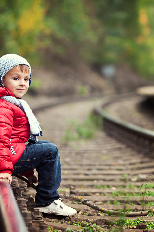 Маленький мальчик в красной куртке сидит на рельсах