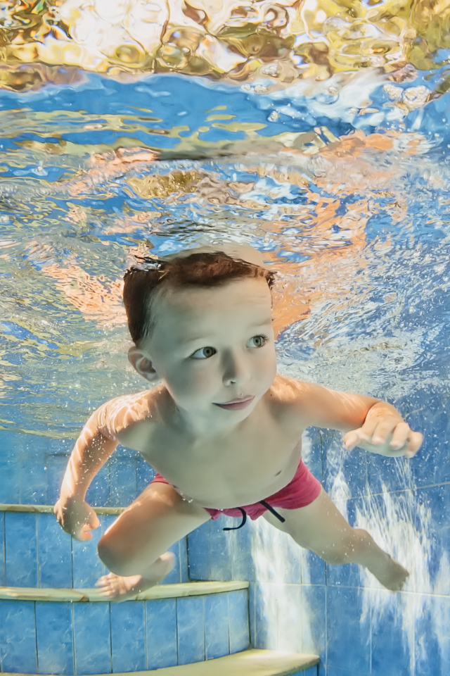 Маленький мальчик плавает под водой в бассейне