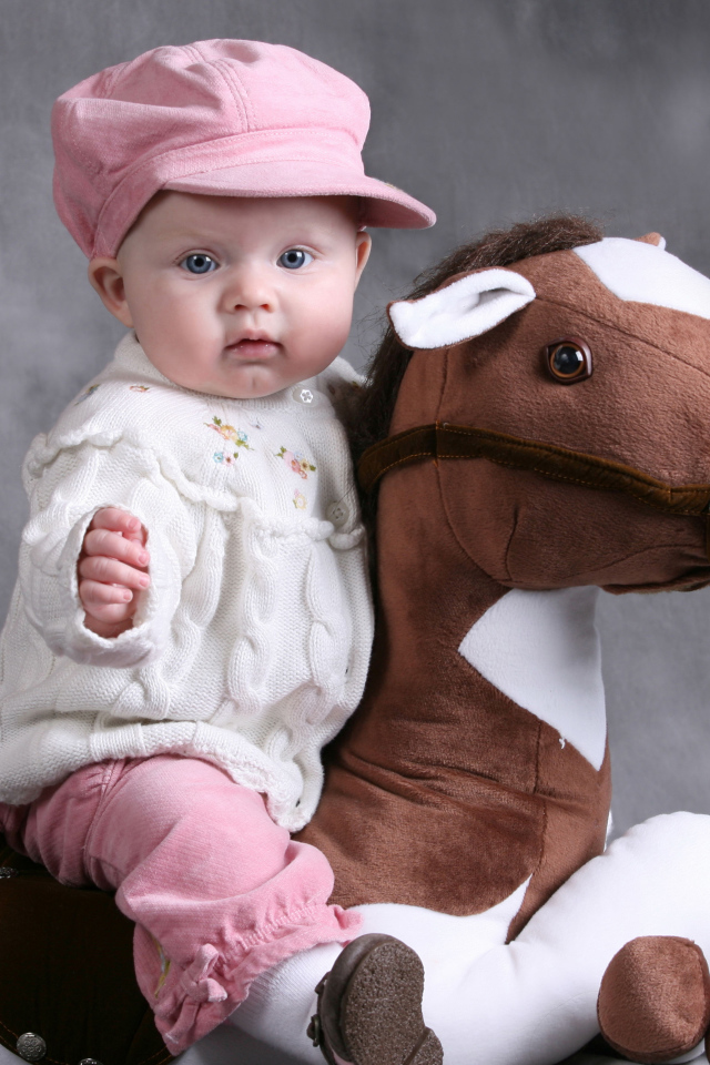 Маленький ребенок в розовой кепке сидит на игрушечной лошади