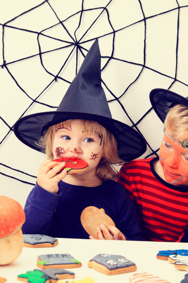 Маленькие дети в костюмах на Хэллоуин едят праздничные сладости
