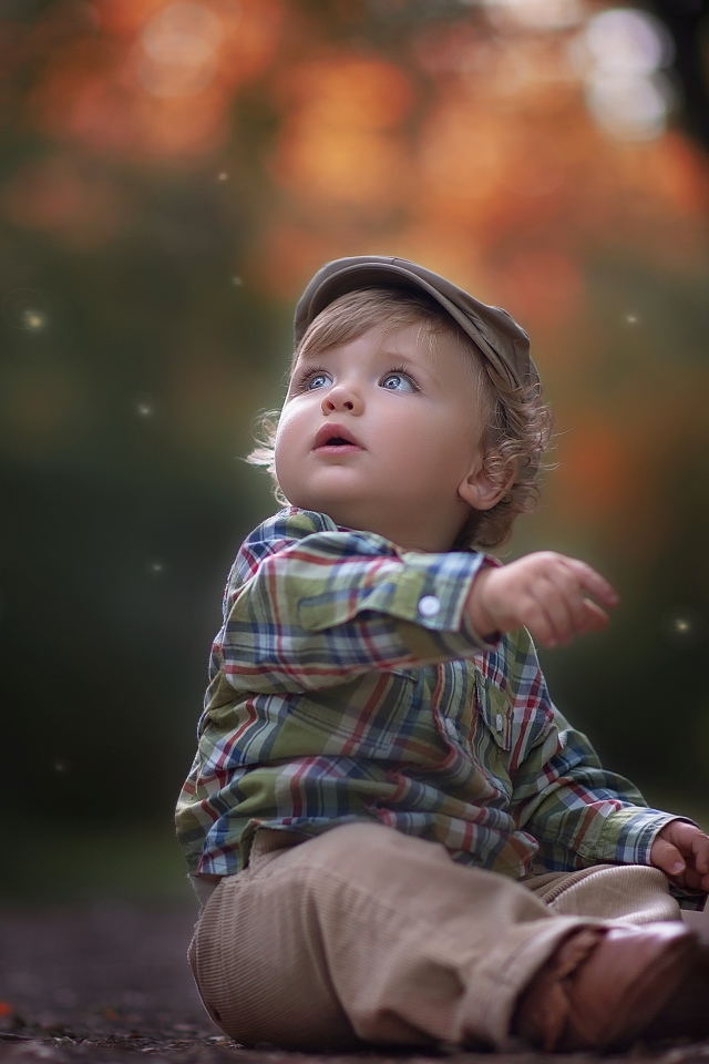 Маленький милый мальчик сидит в кепке на дороге