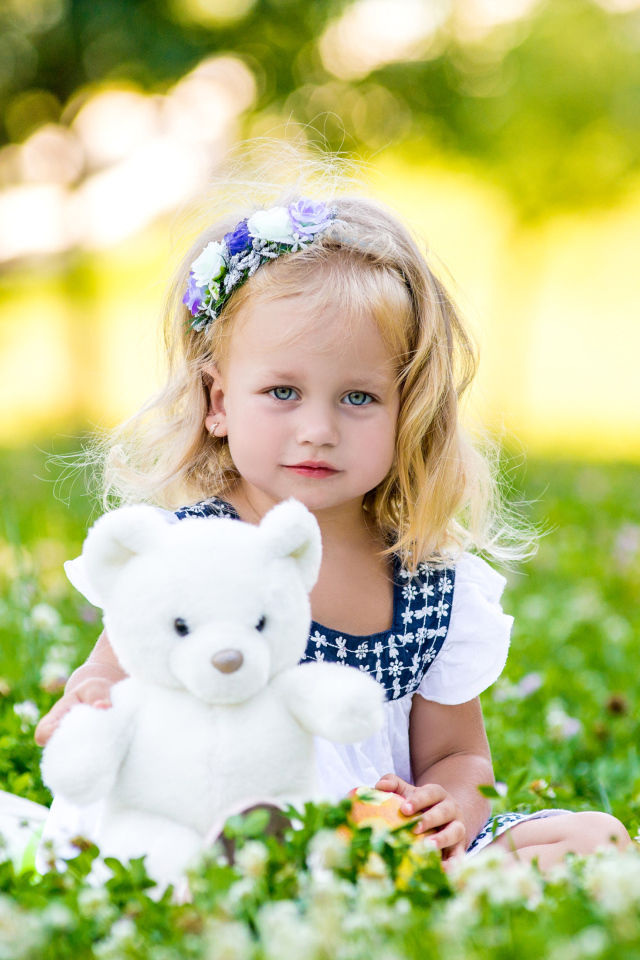 Маленькая милая девочка с игрушкой сидит на зеленой траве с цветами