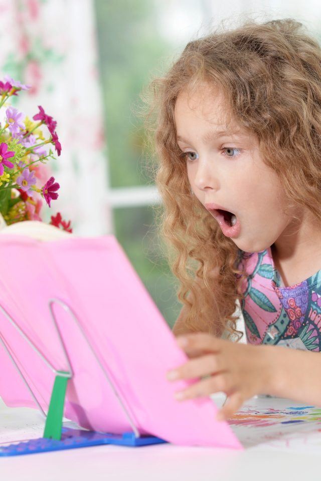 Маленькая русоволосая девочка удивленно смотрит в книгу