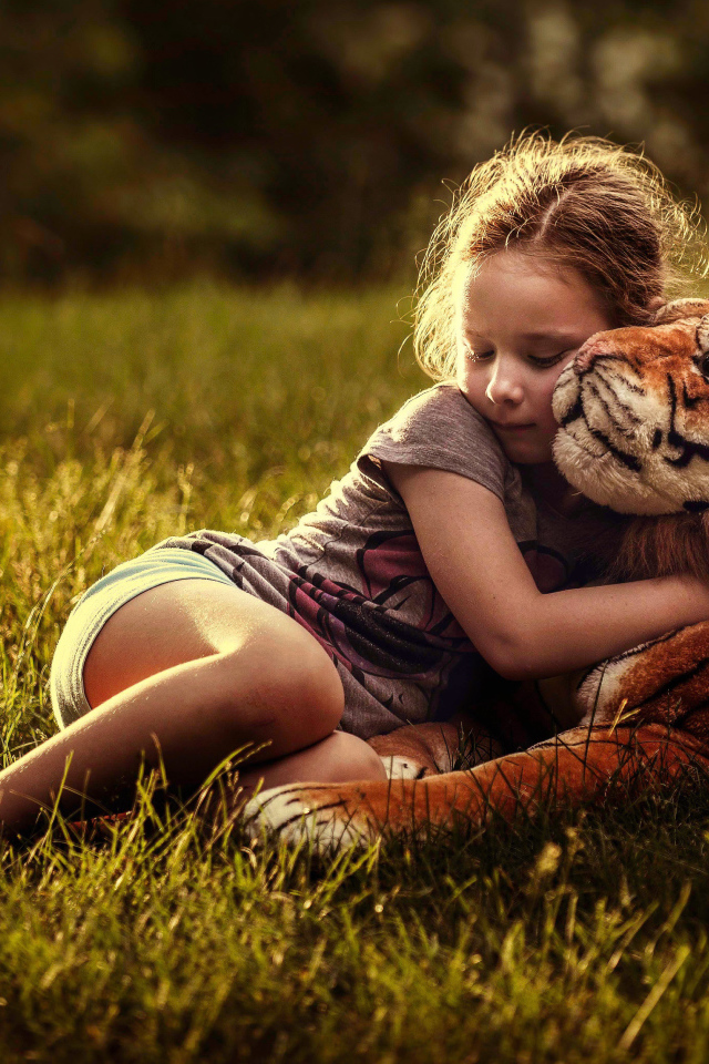 Маленькая девочка обнимает игрушечного тигра на зеленой траве