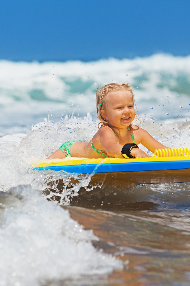 Маленькая девочка в море на доске для серфинга