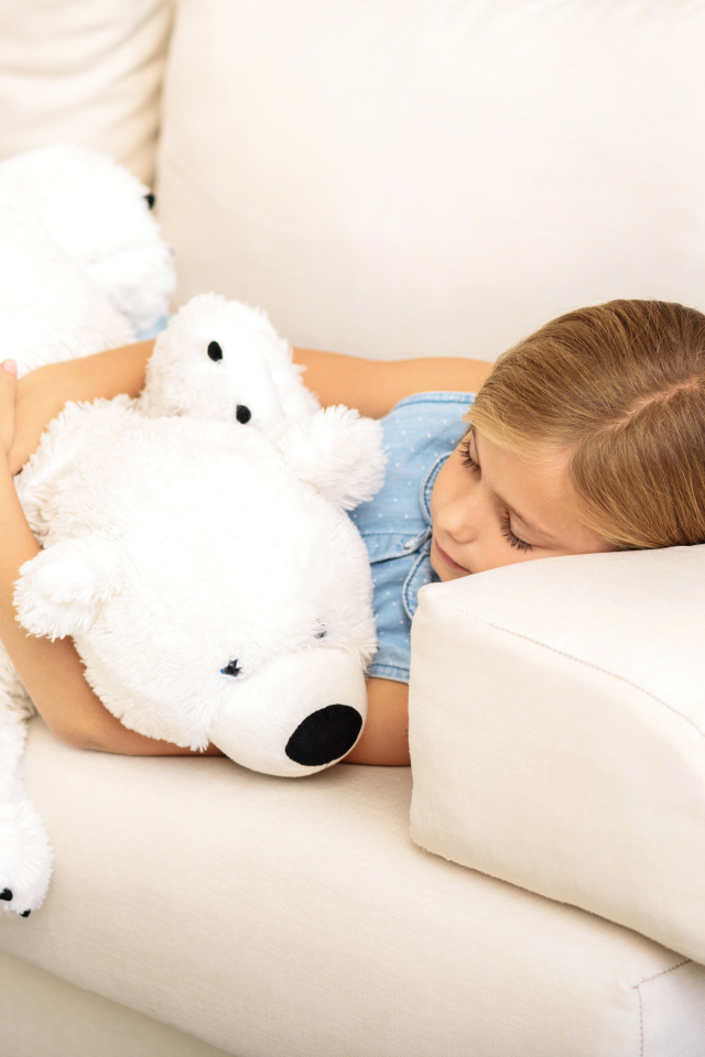 Маленькая девочка спит с белым плюшевым мишкой на диване