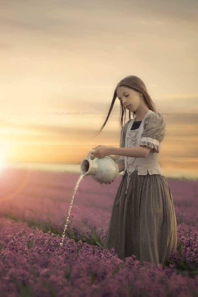 Маленькая девочка поливает цветы из кувшина в поле на закате