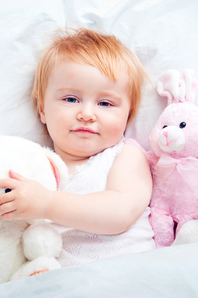 Маленькая девочка лежит в кровати с плюшевыми игрушками