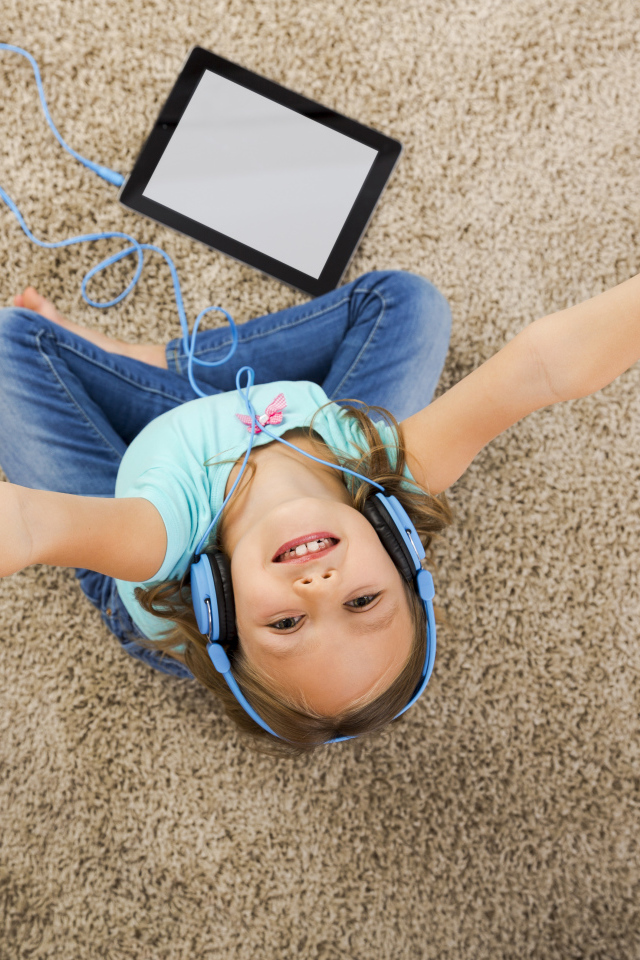 Маленькая девочка слушает музыку в наушниках сидя на ковре